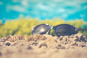 a pair fo sunglasses on a beach with scabble tiles spelling out summer. Perfect vacation.